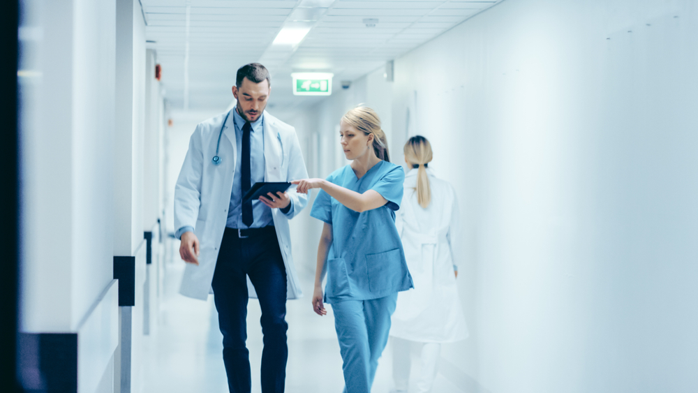 doctor accompanied by colleague walking in hallway whilst looking at tablet