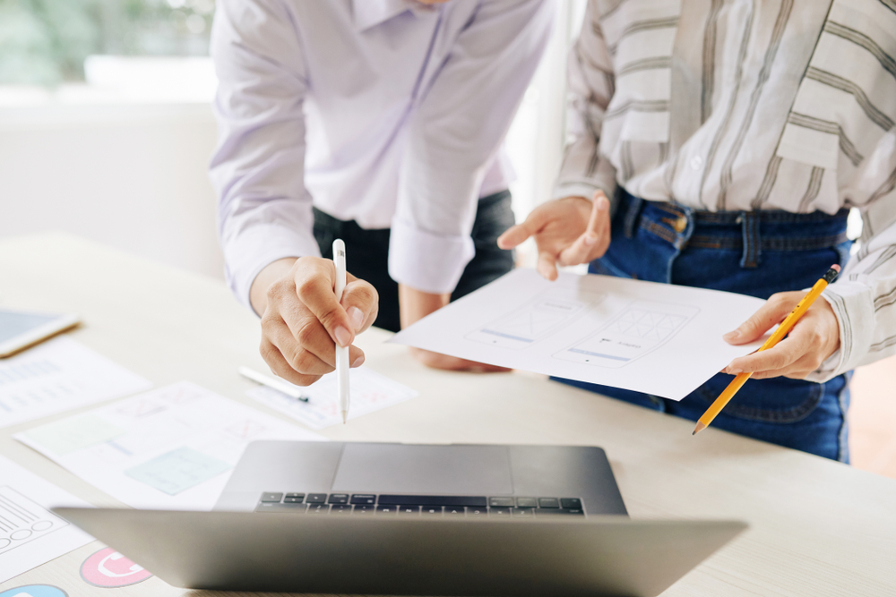 two people looking at data over laptop and sheet whilst holding pen and pencil