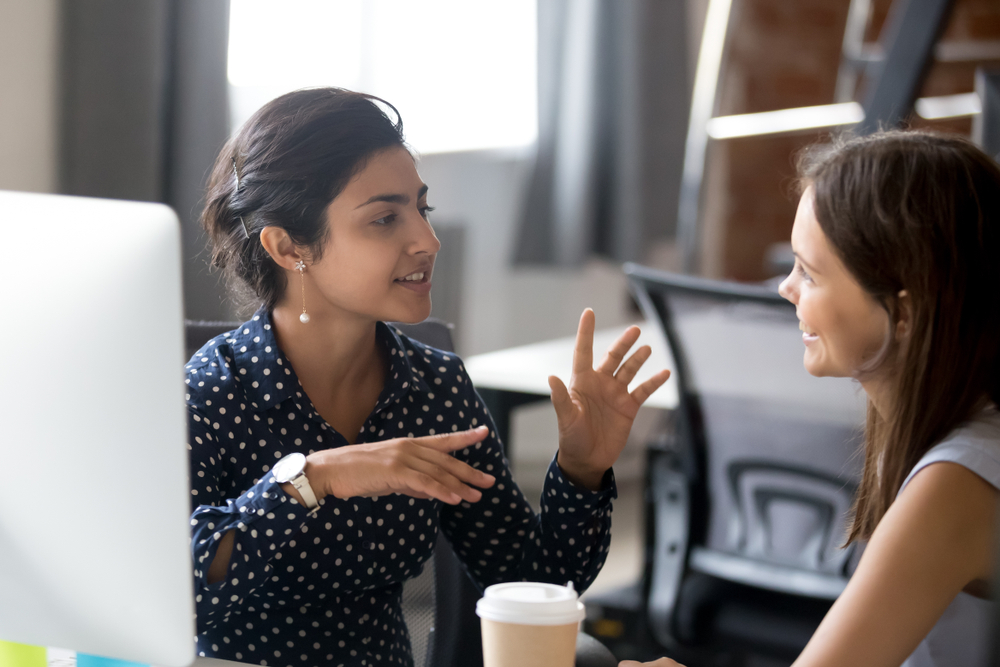 Female in shirt explains to another female colleague gesturing with hands