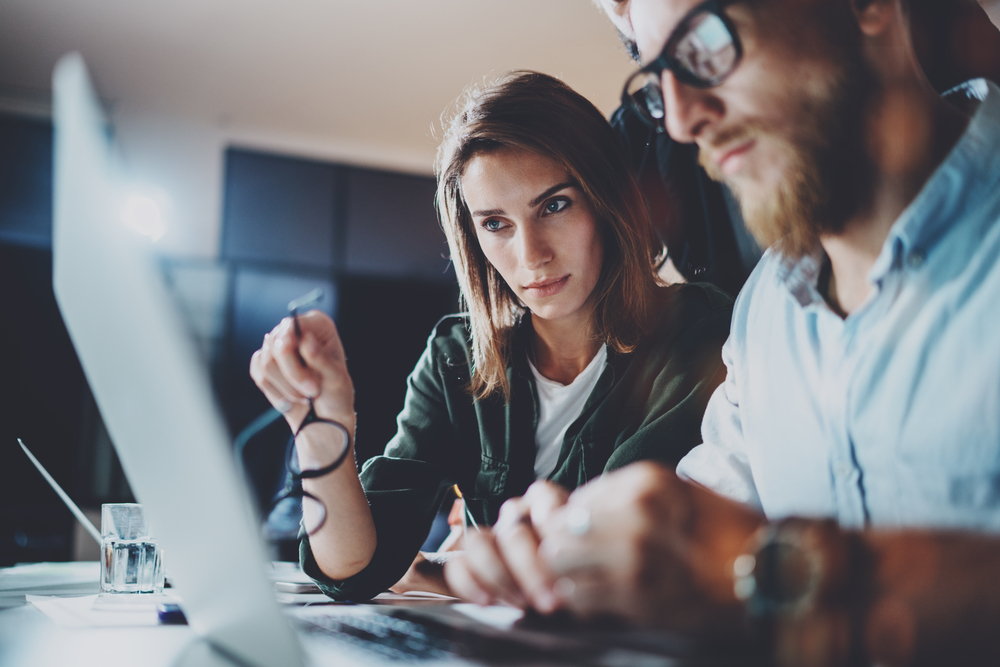 woman holding glasses and looking at her laptop with colleague